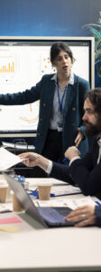 Public relations group creating marketing ad campaigns and promotional activities in a conference room, collaborating on development plan. Specialists reviewing sales trends on interactive board.